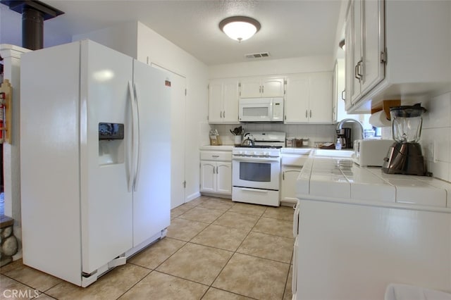 kitchen with decorative backsplash, white appliances, sink, white cabinetry, and tile counters