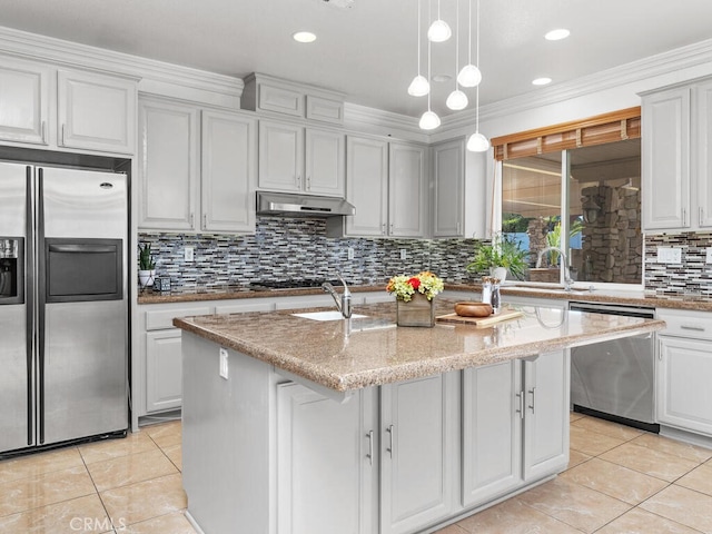 kitchen featuring appliances with stainless steel finishes, light stone counters, ornamental molding, and an island with sink