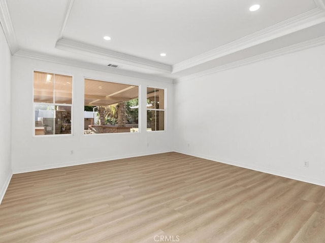 empty room with a raised ceiling, light hardwood / wood-style flooring, and ornamental molding