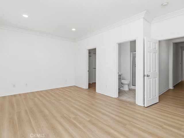 unfurnished bedroom featuring ensuite bath, light hardwood / wood-style floors, a walk in closet, a closet, and ornamental molding