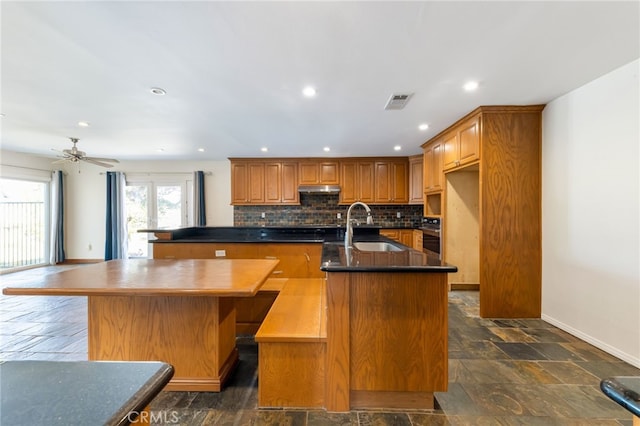 kitchen featuring ceiling fan, sink, an island with sink, and tasteful backsplash