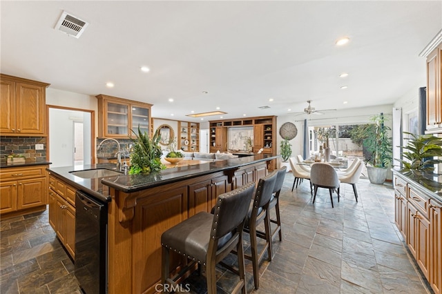 kitchen featuring backsplash, a center island with sink, sink, ceiling fan, and black dishwasher