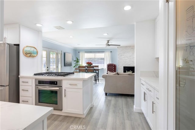 kitchen featuring ceiling fan, light hardwood / wood-style floors, appliances with stainless steel finishes, a stone fireplace, and white cabinets