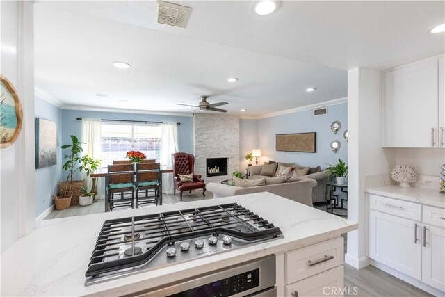 kitchen featuring a fireplace, white cabinetry, light hardwood / wood-style flooring, stainless steel gas cooktop, and light stone counters