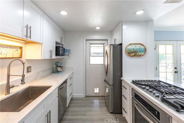 kitchen featuring white cabinetry, stainless steel appliances, light wood-type flooring, a wealth of natural light, and sink