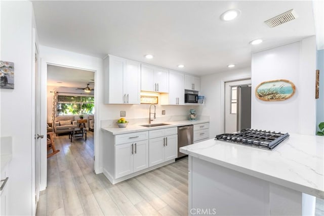 kitchen with white cabinets, stainless steel appliances, sink, light stone counters, and light hardwood / wood-style flooring