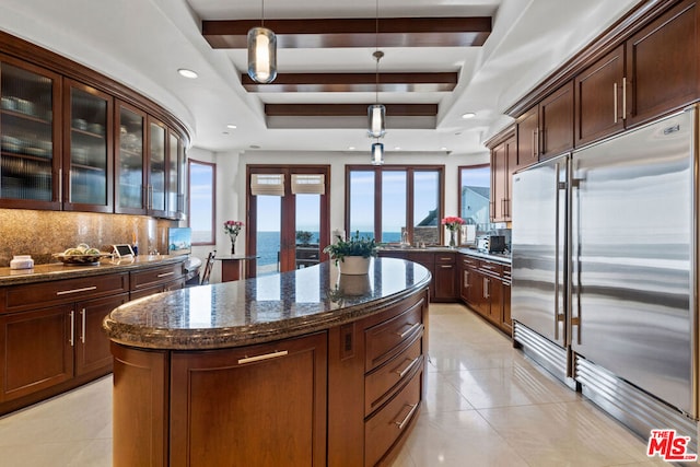 kitchen featuring a raised ceiling, a water view, built in refrigerator, decorative backsplash, and decorative light fixtures