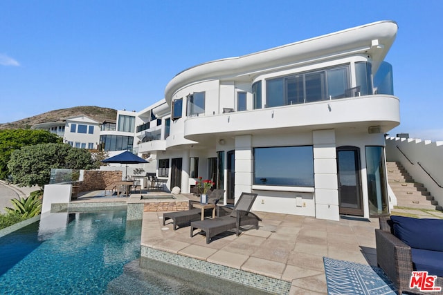 back of house featuring a balcony, a fenced in pool, and a patio