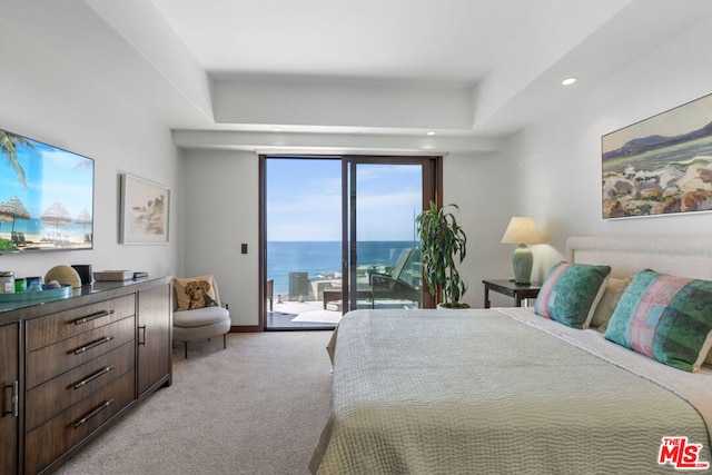 carpeted bedroom featuring a raised ceiling, access to exterior, and a water view