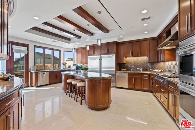 kitchen featuring beam ceiling, appliances with stainless steel finishes, decorative light fixtures, a kitchen island, and a kitchen bar