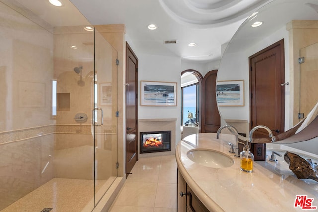 bathroom featuring a multi sided fireplace, tile patterned flooring, vanity, and a shower with shower door