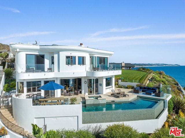 back of property featuring a balcony, a water view, a patio, and a pool with hot tub