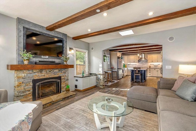 living room with beam ceiling, a stone fireplace, and hardwood / wood-style flooring