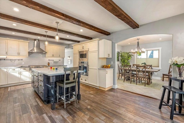 kitchen with appliances with stainless steel finishes, dark hardwood / wood-style flooring, wall chimney range hood, a kitchen island, and pendant lighting