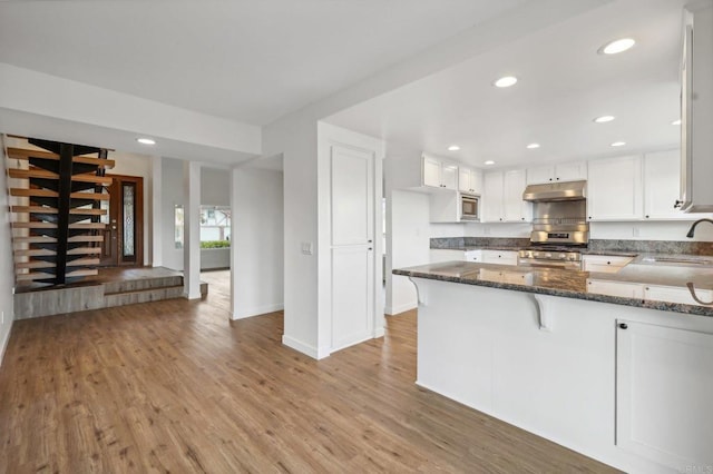 kitchen with white cabinetry, kitchen peninsula, dark stone countertops, appliances with stainless steel finishes, and light wood-type flooring