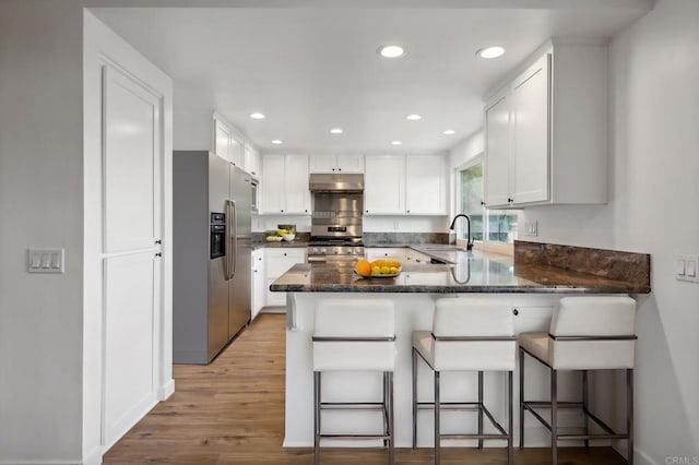 kitchen with white cabinetry, sink, kitchen peninsula, appliances with stainless steel finishes, and light wood-type flooring