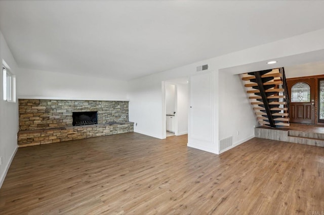 unfurnished living room with light wood-type flooring, a stone fireplace, and a healthy amount of sunlight