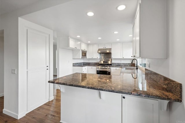 kitchen featuring kitchen peninsula, a kitchen bar, stainless steel appliances, and white cabinets