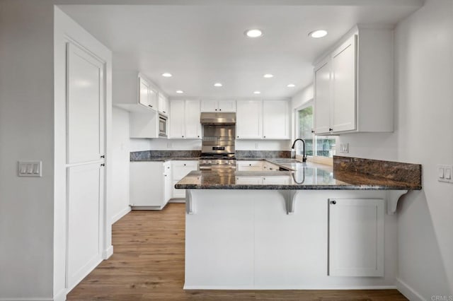 kitchen featuring kitchen peninsula, light wood-type flooring, stainless steel appliances, sink, and white cabinetry