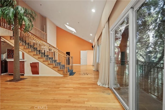 hall featuring wood-type flooring, a skylight, and high vaulted ceiling