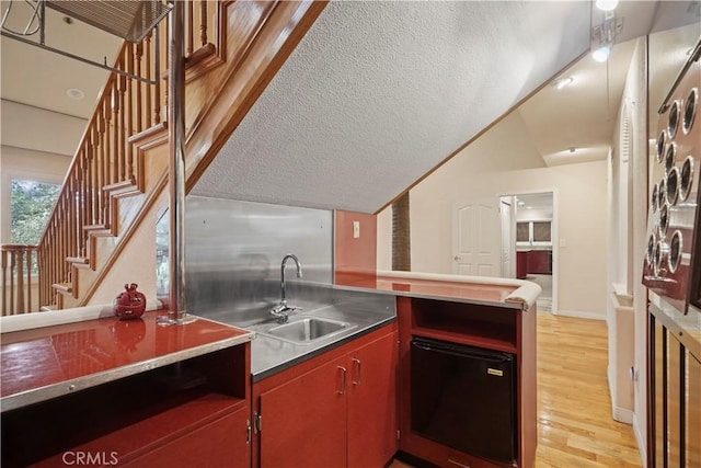 kitchen featuring stainless steel counters, sink, a textured ceiling, and light wood-type flooring