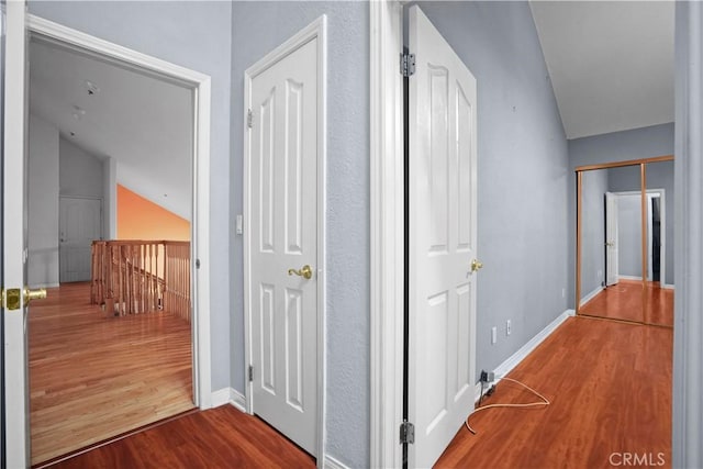 hall with wood-type flooring and vaulted ceiling