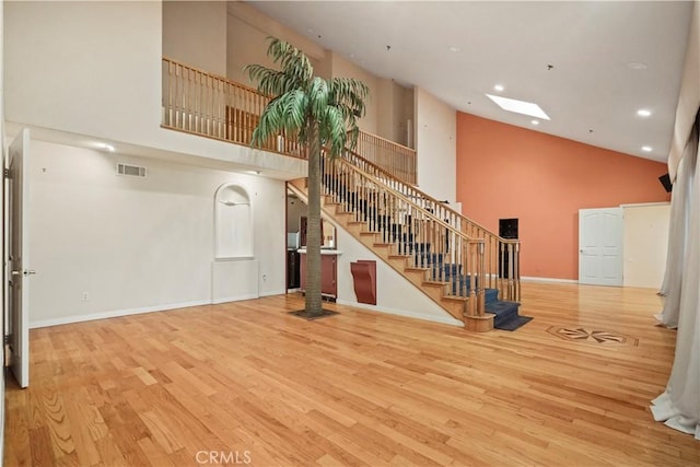 unfurnished living room with a skylight, light hardwood / wood-style flooring, and high vaulted ceiling