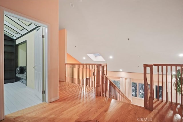 hallway with lofted ceiling with skylight and light wood-type flooring