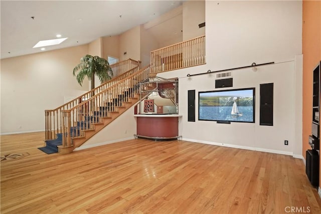 unfurnished living room with a skylight, high vaulted ceiling, and light hardwood / wood-style floors