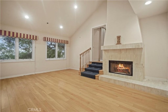 unfurnished living room with a large fireplace, light wood-type flooring, and high vaulted ceiling