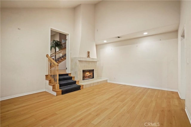 living room featuring a tiled fireplace, high vaulted ceiling, and light hardwood / wood-style flooring