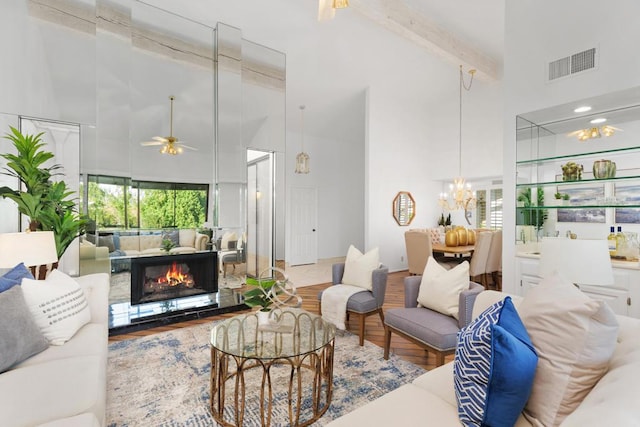 living room with beamed ceiling, ceiling fan with notable chandelier, wood-type flooring, and high vaulted ceiling