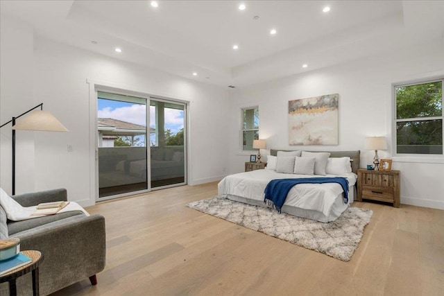 bedroom featuring access to outside, a tray ceiling, and light hardwood / wood-style floors