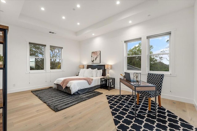 bedroom with a tray ceiling and light wood-type flooring