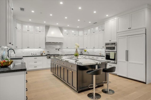 kitchen featuring white cabinets, a center island, sink, and premium range hood