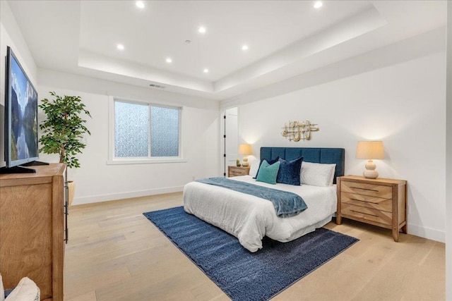 bedroom featuring a raised ceiling and light hardwood / wood-style flooring