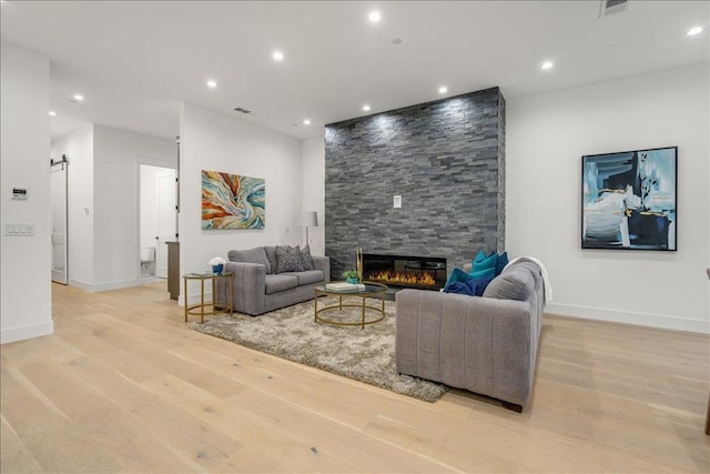 living room featuring a barn door, a stone fireplace, and light wood-type flooring