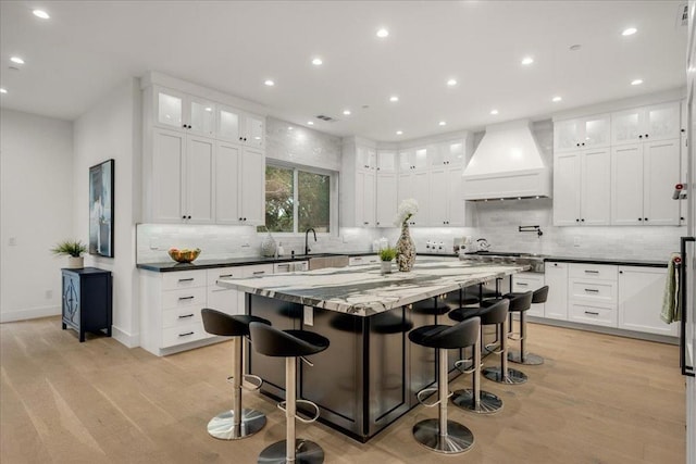 kitchen featuring a kitchen breakfast bar, custom exhaust hood, a spacious island, and light hardwood / wood-style flooring