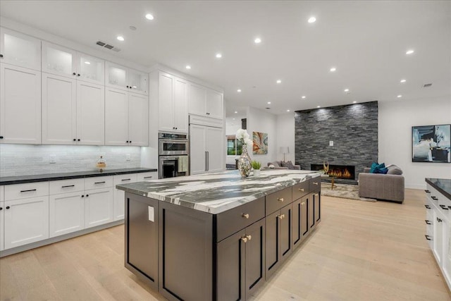 kitchen with appliances with stainless steel finishes, a fireplace, a spacious island, light hardwood / wood-style flooring, and white cabinets