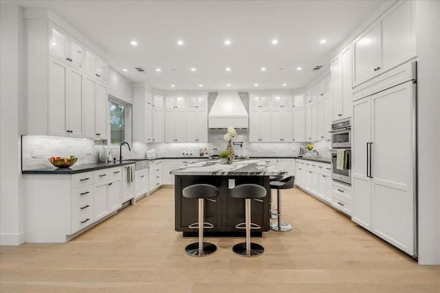 kitchen with custom exhaust hood, a kitchen island, light hardwood / wood-style floors, white cabinetry, and a breakfast bar area