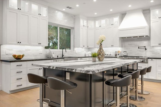 kitchen featuring premium range hood, a kitchen island, white cabinets, and a breakfast bar area