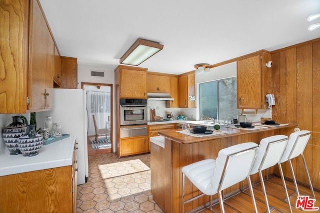 kitchen with black electric stovetop, oven, a kitchen breakfast bar, light hardwood / wood-style flooring, and kitchen peninsula