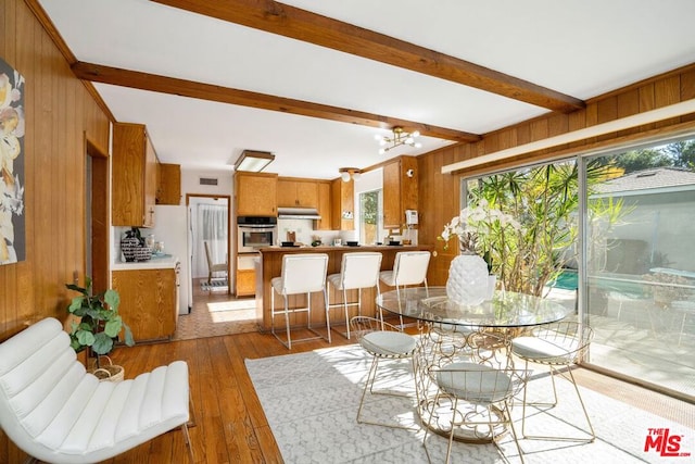 dining area featuring beamed ceiling, wooden walls, dark wood-type flooring, and a notable chandelier