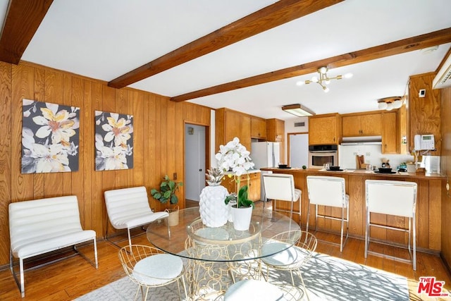 dining area featuring hardwood / wood-style flooring, a notable chandelier, beam ceiling, and wooden walls