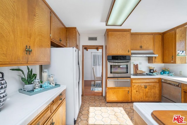 kitchen featuring appliances with stainless steel finishes, tasteful backsplash, tile counters, and light tile patterned flooring