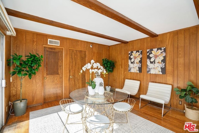 dining space featuring wooden walls, beamed ceiling, and wood-type flooring