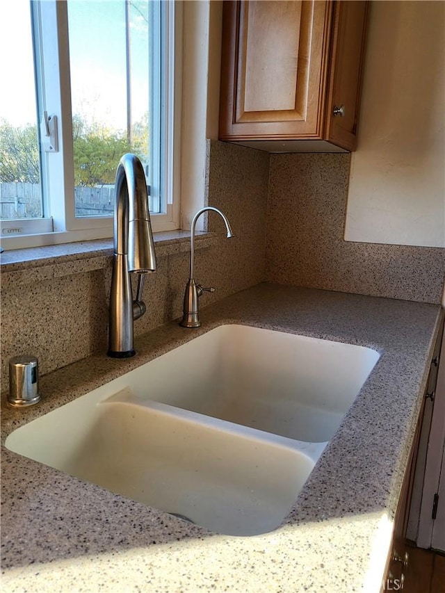 details featuring backsplash, light stone counters, and sink