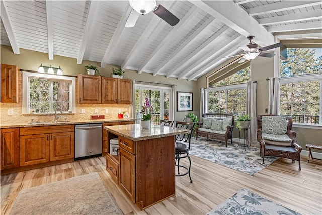 kitchen with sink, dishwasher, backsplash, a center island, and light stone countertops