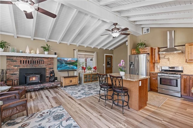 kitchen with appliances with stainless steel finishes, a center island, light stone countertops, and wall chimney range hood