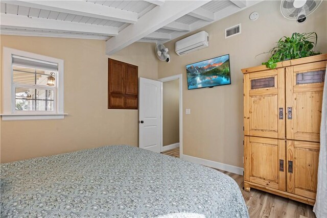 bedroom featuring lofted ceiling with beams, a wall unit AC, and light hardwood / wood-style flooring